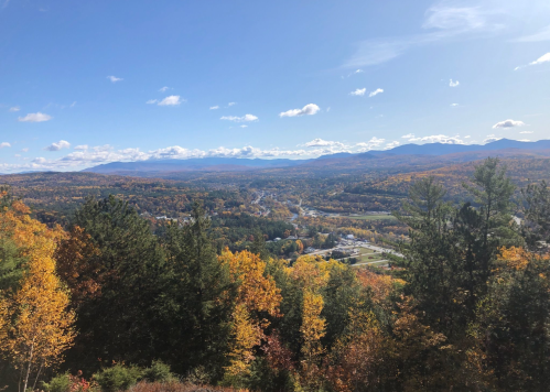 A scenic view of rolling hills and valleys covered in vibrant autumn foliage under a clear blue sky.