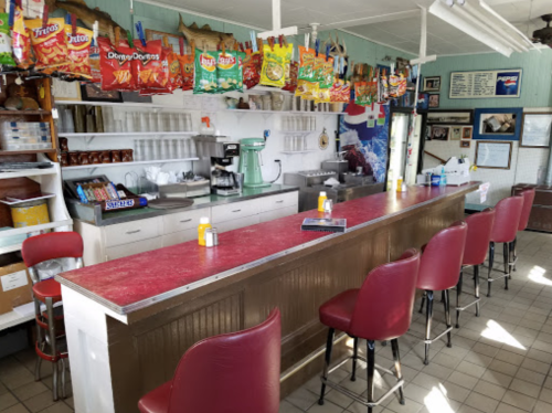 A retro diner interior with a red countertop, bar stools, and colorful snack bags hanging above the counter.