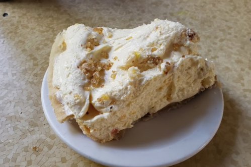 A slice of creamy dessert topped with crushed nuts on a small white plate.