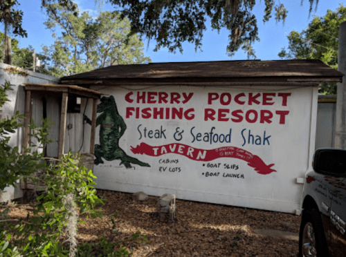 Sign for Cherry Pocket Fishing Resort featuring a gator graphic, promoting a steak and seafood shack, cabins, and boat launch.