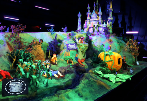 Colorful display featuring a whimsical landscape with a castle, characters, and vibrant plants, illuminated with neon lights.