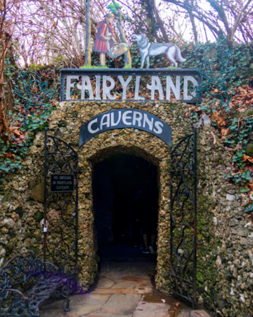 Entrance to Fairyland Caverns, featuring a stone archway and whimsical decorations, surrounded by trees and foliage.