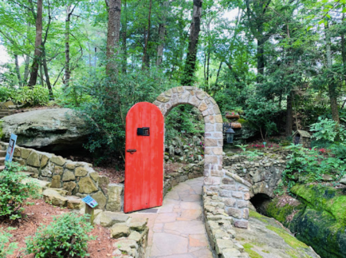 A vibrant red door in a stone archway, surrounded by lush greenery and a winding path in a serene garden setting.