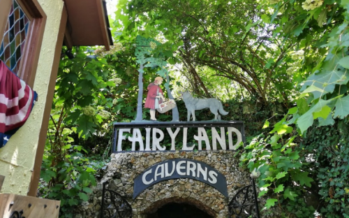 Sign for "Fairyland Caverns" with a figure and a dog, surrounded by lush green foliage.