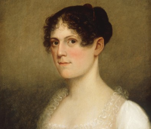 Portrait of a woman with curly hair, wearing a white dress, gazing directly at the viewer with a soft expression.