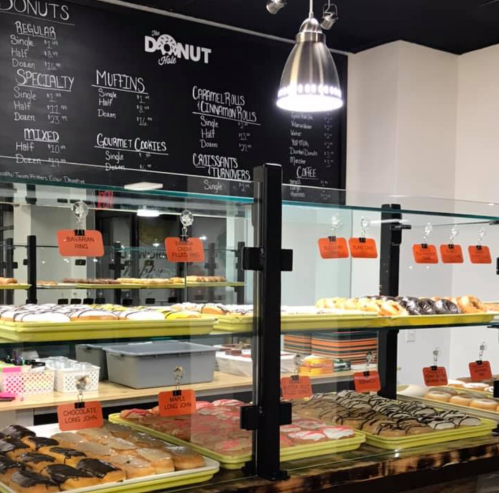 A display case filled with various donuts and pastries, with a menu board in the background listing options.