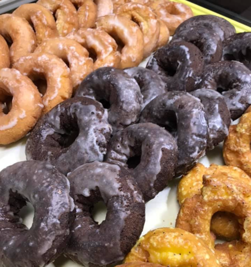 A tray of assorted donuts, including glazed, chocolate, and cake varieties, arranged in rows.