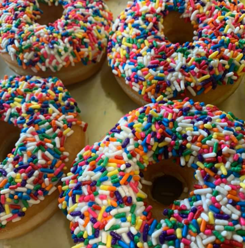 Four colorful donuts covered in vibrant sprinkles on a light background.
