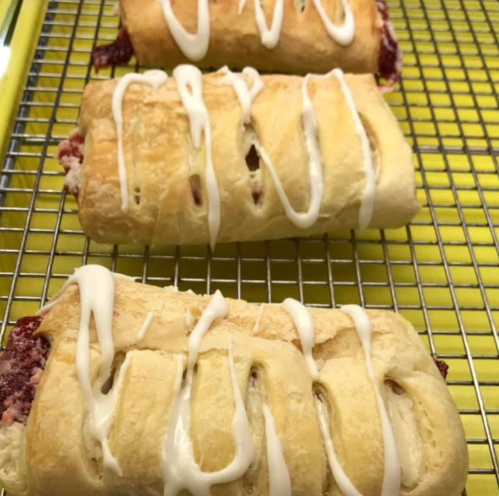 Three freshly baked pastries drizzled with white icing, resting on a yellow cooling rack.