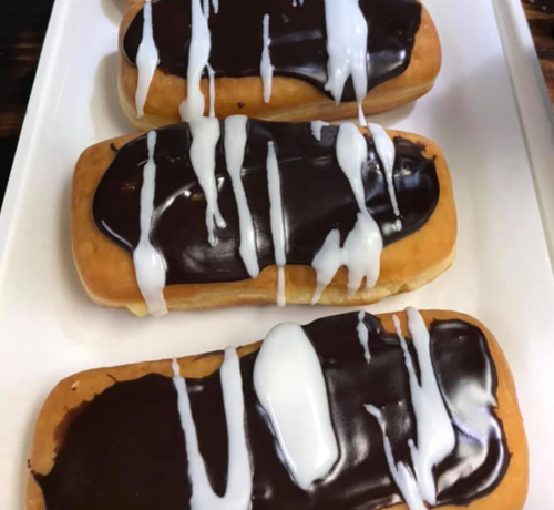 Three rectangular donuts topped with chocolate icing and white drizzle, arranged on a white plate.