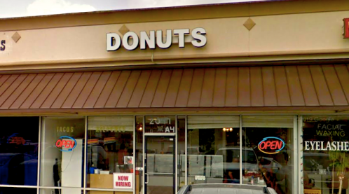 Storefront featuring a "DONUTS" sign, with "OPEN" neon lights and a "NOW HIRING" sign in the window.