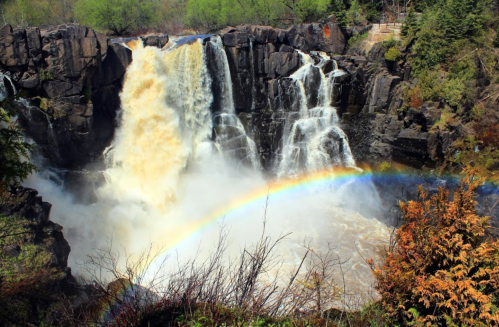 A powerful waterfall cascades over rocky cliffs, with a vibrant rainbow arching over the misty water below.