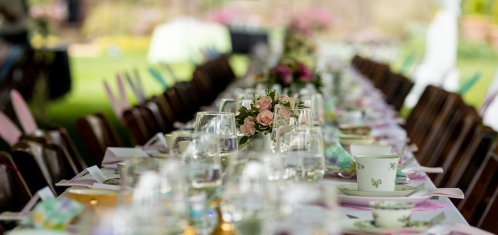 A beautifully set outdoor dining table with floral centerpieces and elegant tableware, surrounded by chairs.