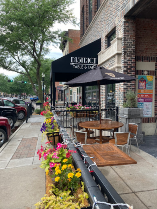 Outdoor seating area of a restaurant with colorful flowers, tables, and an awning that reads "District Table & Tap."