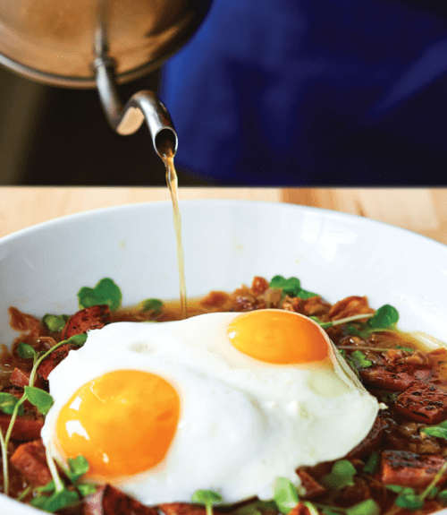A bowl of savory dish topped with two sunny-side-up eggs, with broth being poured over it.
