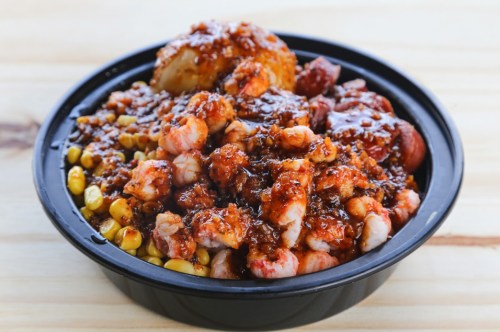 A black bowl filled with shrimp, sausage, corn, and a rich, spicy sauce.