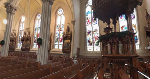 Interior of a church featuring wooden pews, ornate carvings, and colorful stained glass windows.
