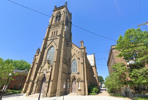 Historic church with a tall tower, surrounded by trees and clear blue sky, set in an urban environment.