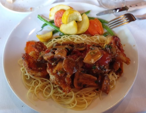 A plate of spaghetti topped with chicken, mushrooms, and a medley of colorful vegetables on the side.