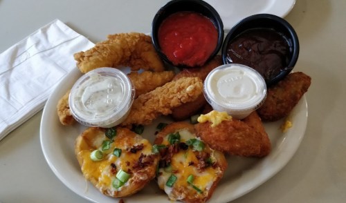 A plate of fried chicken strips, stuffed potato skins topped with cheese, and dipping sauces.