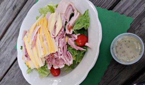 A plate of salad with lettuce, sliced turkey, cheese, cherry tomatoes, and a small container of dressing on the side.