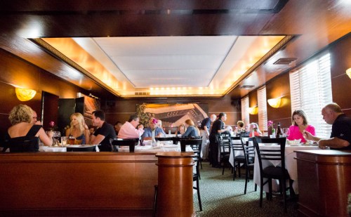 A bustling restaurant interior with diners at tables, warm lighting, and elegant decor.