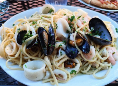 A plate of seafood pasta with shrimp, mussels, and calamari, garnished with parsley on a black table.