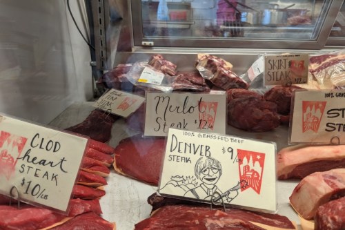Display of various cuts of beef steaks with price tags, including Merlot and Denver steaks, in a butcher shop.