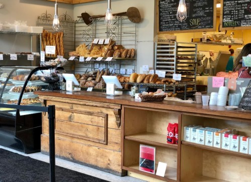 A cozy bakery display with various breads and pastries, featuring a wooden counter and chalkboard menu in the background.