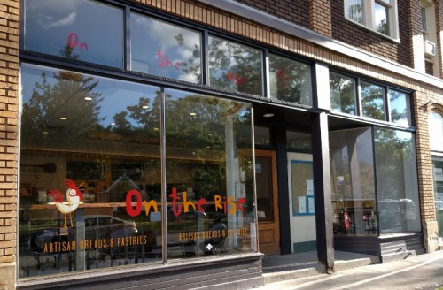 A bakery storefront with large windows, featuring the name "On the Rise" and a chicken graphic.