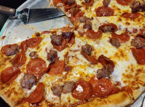A close-up of a pepperoni and sausage pizza on a metal tray, with a slice partially removed.