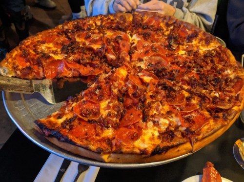 A large pizza topped with pepperoni and sausage, with a slice removed, served on a metal tray.