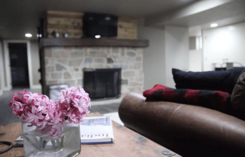 Cozy living room with a stone fireplace, a leather couch, and a vase of pink flowers on a wooden table.