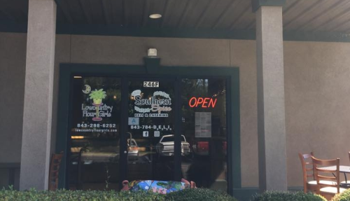 Front entrance of a restaurant with "Open" sign, featuring glass doors and outdoor seating.