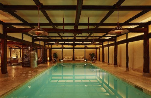 A serene indoor pool area with wooden beams, soft lighting, and comfortable seating, creating a tranquil atmosphere.
