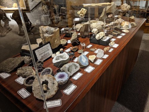 Display of various rocks and minerals in a glass case, labeled with names and descriptions.