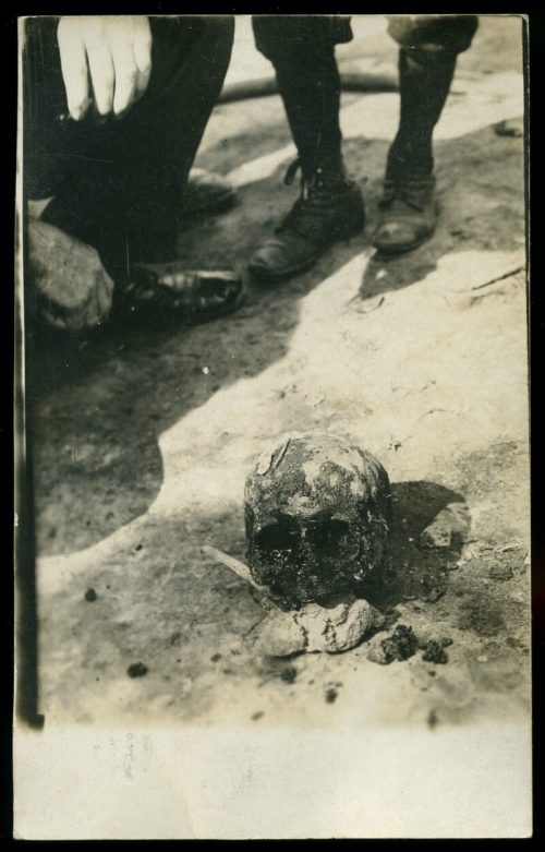 A close-up of a skull on the ground, with two pairs of boots visible in the background.