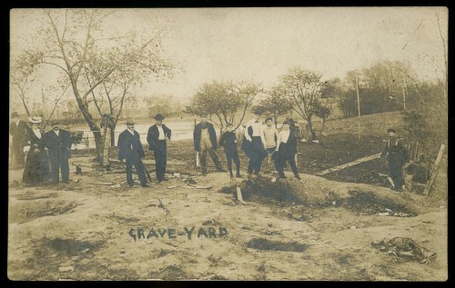 A historical black-and-white photo of a group of people gathered around a grave site in a cemetery.