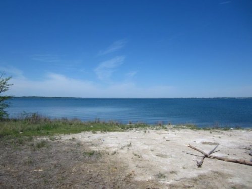 A serene lake view with clear blue water, a sandy shore, and a bright blue sky with wispy clouds.