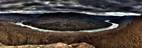 A panoramic view of a winding river surrounded by dark, rugged hills under a cloudy sky.