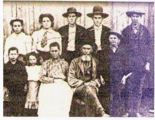 A vintage black-and-white photo of a group of ten people, including men, women, and children, posed outdoors.