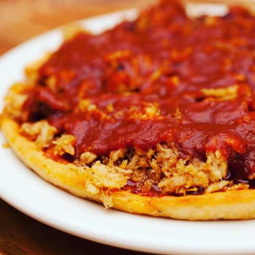 A close-up of a pizza topped with shredded meat and a rich red sauce on a golden crust, served on a white plate.