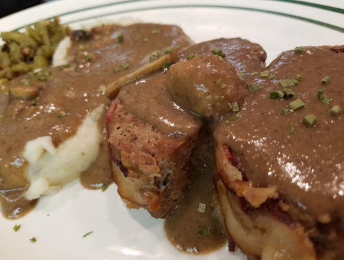 A plate featuring meatloaf with gravy, mashed potatoes, and green beans, garnished with herbs.
