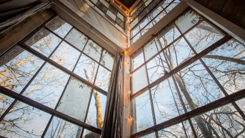 A corner of a room with large windows, showing trees outside and soft lighting along the edges.