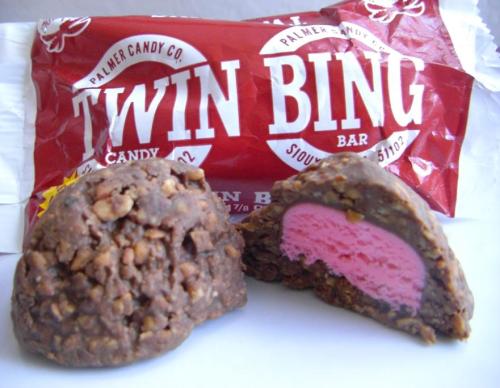 A Twin Bing candy bar, partially cut open, revealing a pink center surrounded by chocolate and crunchy coating.