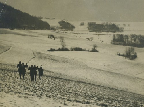 A group of soldiers walks through a snowy landscape, with rolling hills and trees in the background.