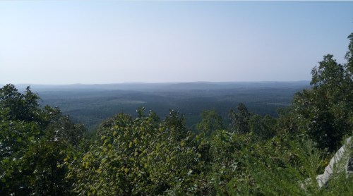 A panoramic view of rolling green hills and distant mountains under a clear blue sky.