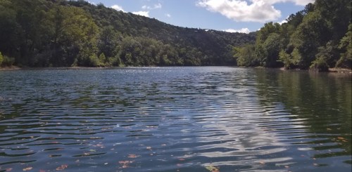 A serene lake surrounded by lush green trees under a partly cloudy sky, with gentle ripples on the water's surface.