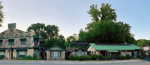 A row of charming buildings with stone facades and greenery, featuring signs for "Boardwalk" and "Tina's Cabin."