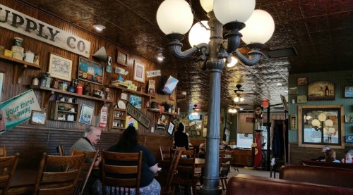 A cozy restaurant interior with vintage decor, wooden tables, and a decorative lamp, featuring patrons enjoying their meals.